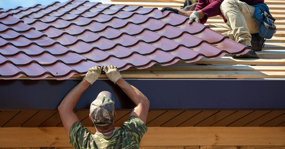 two roofers on a residential roof installing a new metal roofing panel