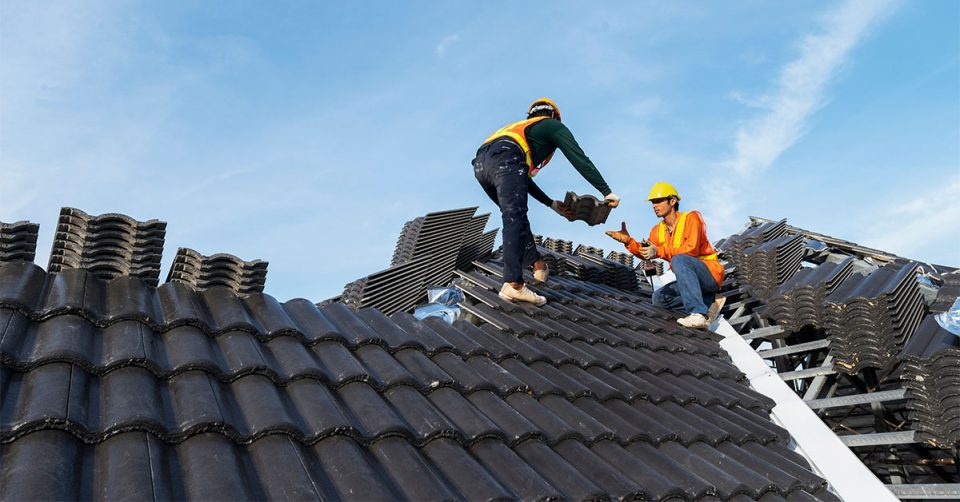 roofer handing roofing materials to another roofer on a roof