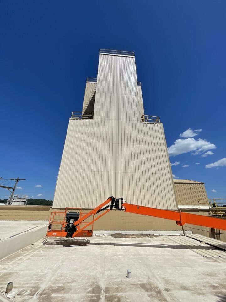 Orange crane in front of yellow agriculture building with roof damage on a partly cloudy day