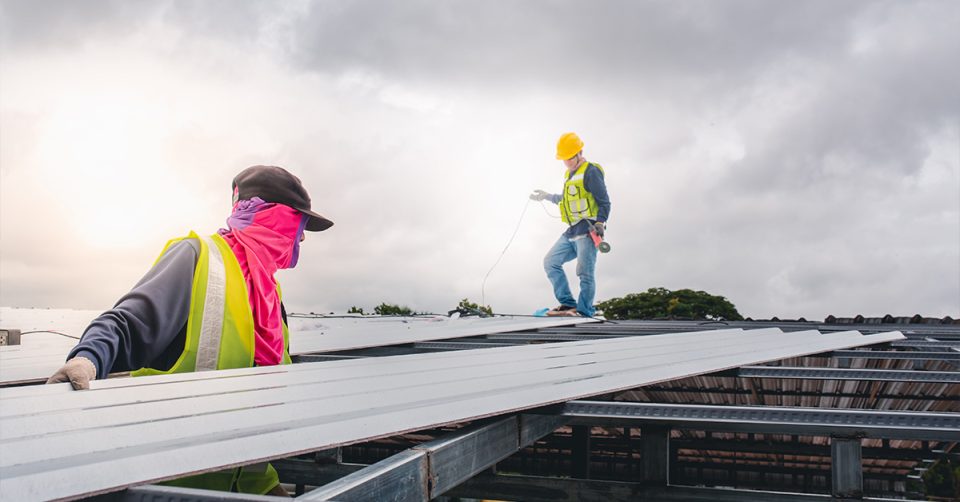 two roofing contractors installing metal roofing panels on a cloudy day